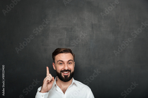 Cropped image of brunette businessman posing on camera with showing index finger up, meaning have idea or just remeber over dark gray background photo
