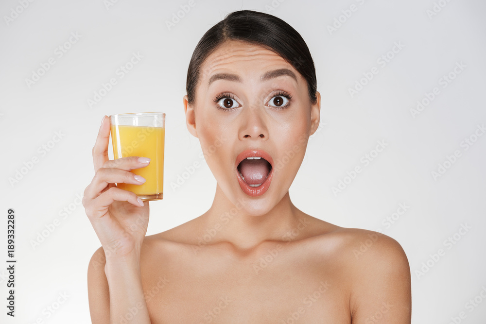 Amusing photo of funny woman with dark hair in bun holding transparent glass of fresh-squeezed orange juice, isolated over white wall Amusing photo of funny woman with dark hair in bun holding transparent glass of fresh-squeezed orange juice, isolated over white wall