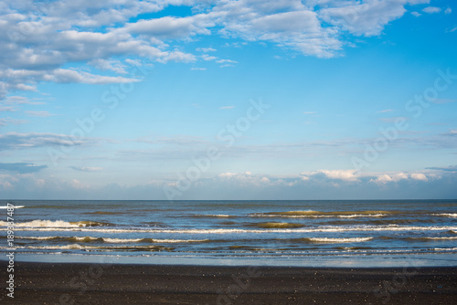seascapes of a beach with foaming waves on the sea, clouds on the horizon
