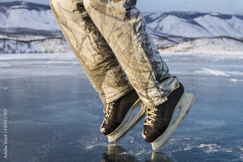 Canvas Print A skater man in black skates in winter warm ski pants shows a moon walk on the clear blue ice of the sacred Lake Baikal in winter on a mountain and sky background