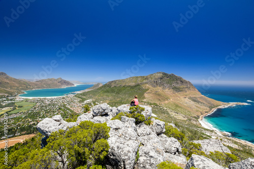 Rear view of young female hiker woman looking at Hout Bay near Cape Town, South Africa, seen from the summit of Little Lion`s Head Mountain. Sandy Bay Beach near Llandudno on the right. photo