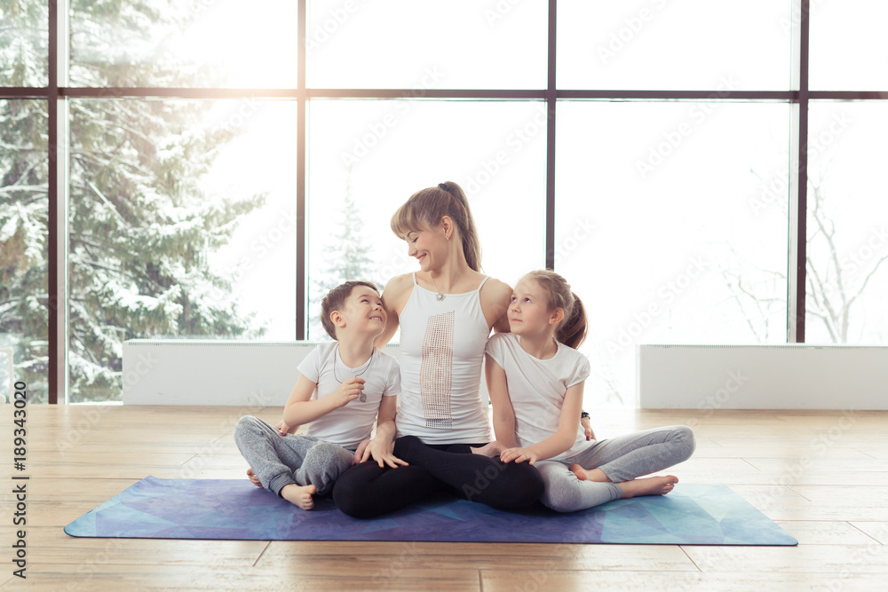 Young family of mother and children son and daughter are engaged in fitness, yoga, exercise in the gym at the winter resort with a beautiful scenery outside the window. Healthy sport lifestyle concept Young family of mother and children son and daughter are engaged in fitness, yoga, exercise in the gym at the winter resort with a beautiful scenery outside the window. Healthy sport lifestyle concept
