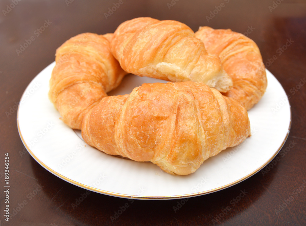 Fresh and tasty croissant in white plate on wood background