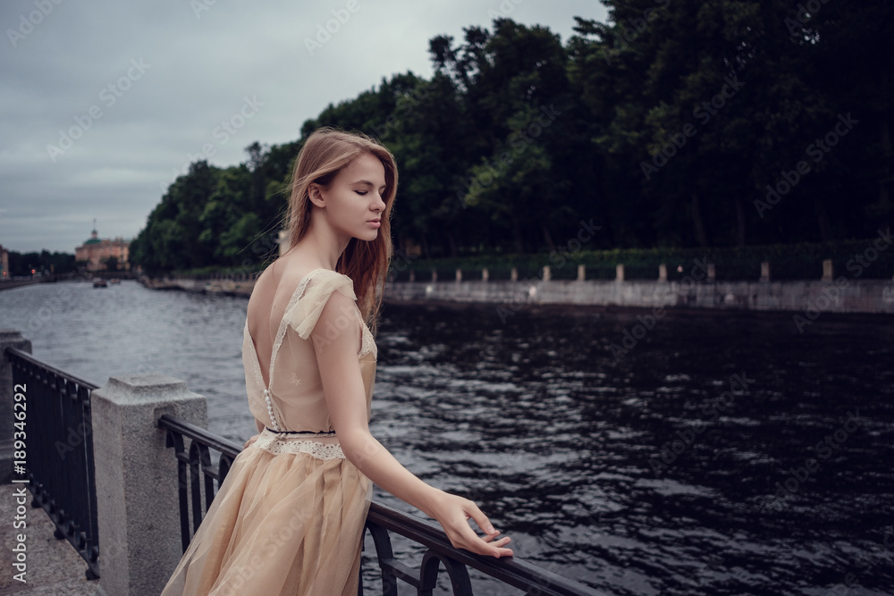 A young red-haired girl in a delicate peach dress is walking along a beautiful old town. St.Petersburg