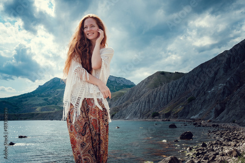 Beautiful boho styled model wearing white crochet swimsuit posing on the beach in sunlight