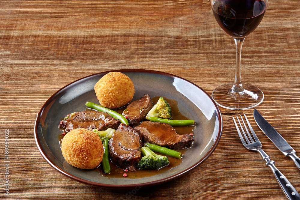 Beef cheeks in sauce with broccoli and green beans on a plate.