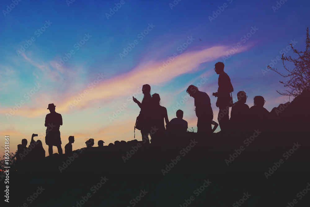 Silhouettes of people standing on the hill watching city on dusk