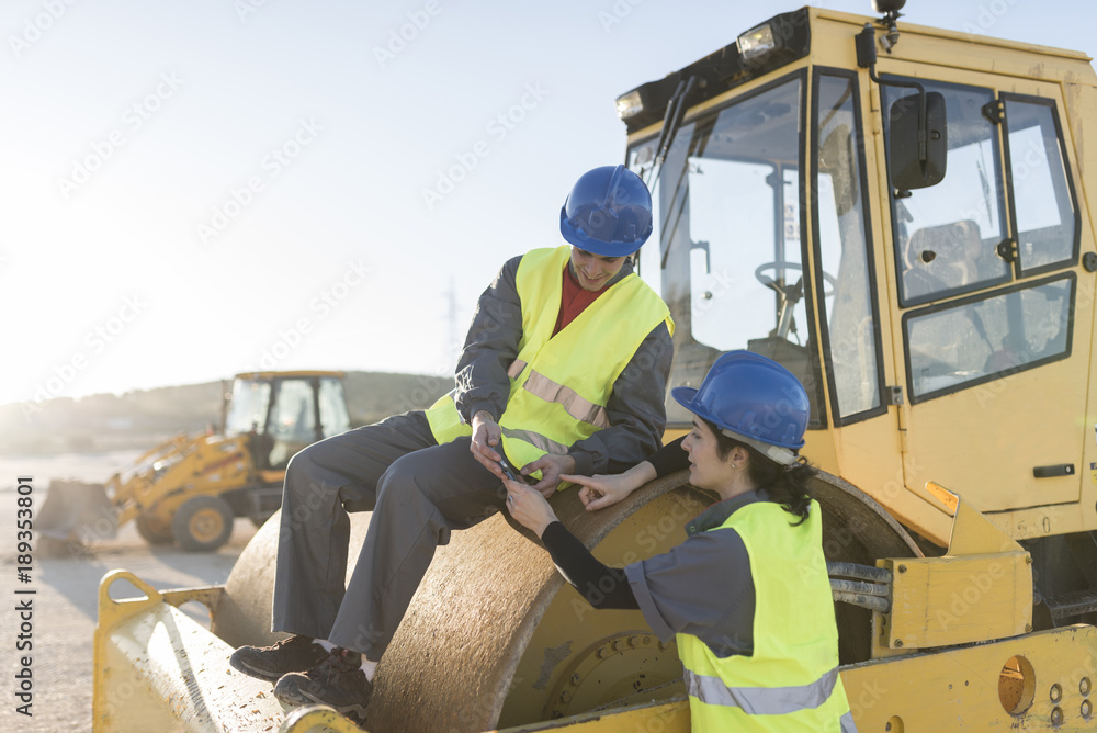 Couple of workers taking a break in their job and looking telephone on steamroller bulldozer