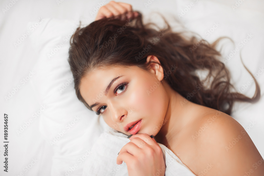 Looking into the camera. Young woman sleeping on the white bed .Top view. Looking into the camera. Young woman sleeping on the white bed .Top view.