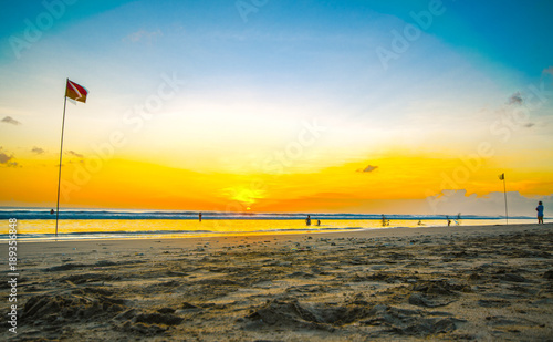 Sunset in an orange, yellow, and blue sky, reflecting on the ocean as the waves crash on the beach © Scott