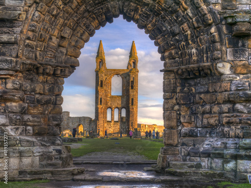 Fotografija The sun shining on the ruins of St Andrews Cathedral viewed through the archway