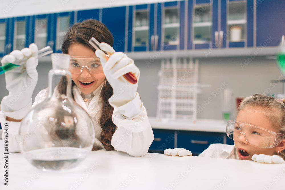 Two little kids in lab coat learning chemistry in school