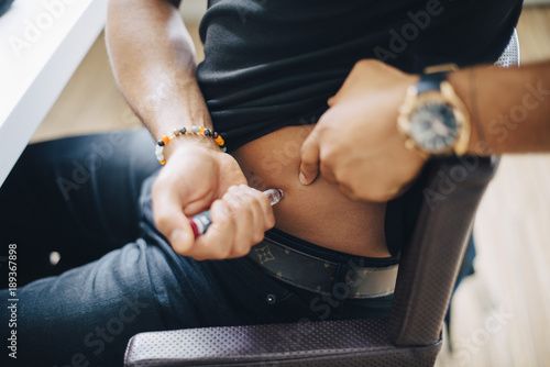 Midsection of businessman injecting insulin in abdomen while sitting at table in office photo