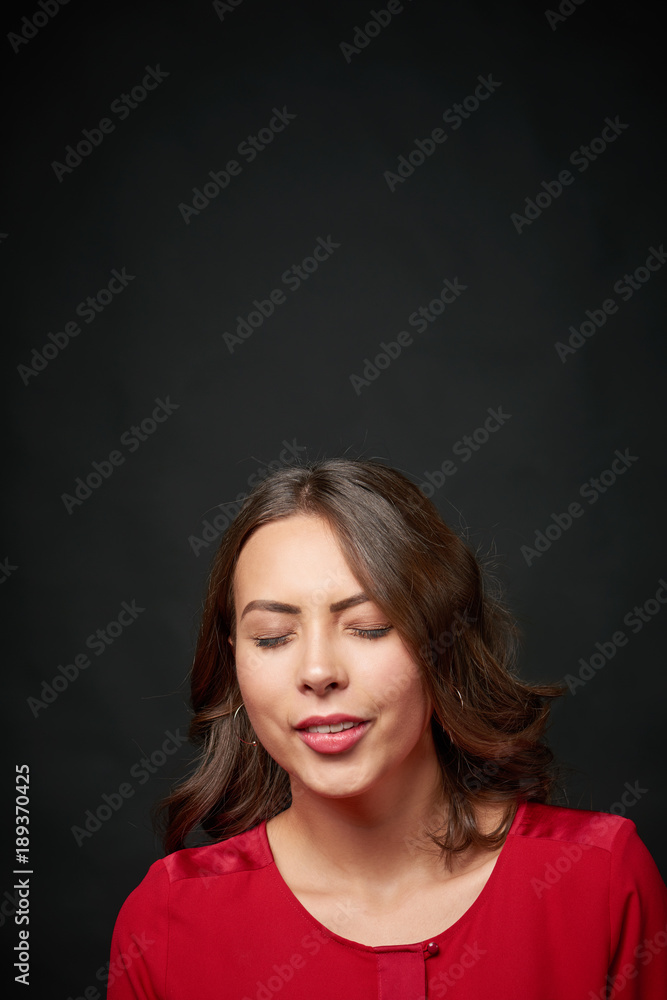 Woman in red shirt and wavy hair making a wish with closed eyes, over dark background, blank copy space above Woman in red shirt and wavy hair making a wish with closed eyes, over dark background, blank copy space above