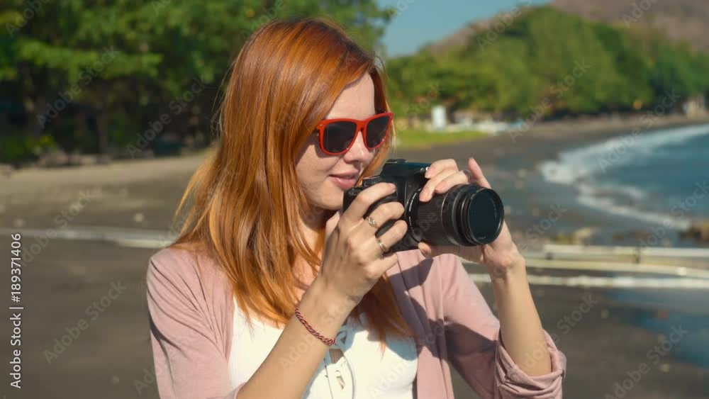 Young caucasian woman in sunglasses taking photo with reflex camera on volcanic sand beach in Pemuteran and smiling on sunny summer day Young caucasian woman in sunglasses taking photo with reflex camera on volcanic sand beach in Pemuteran and smiling on sunny summer day