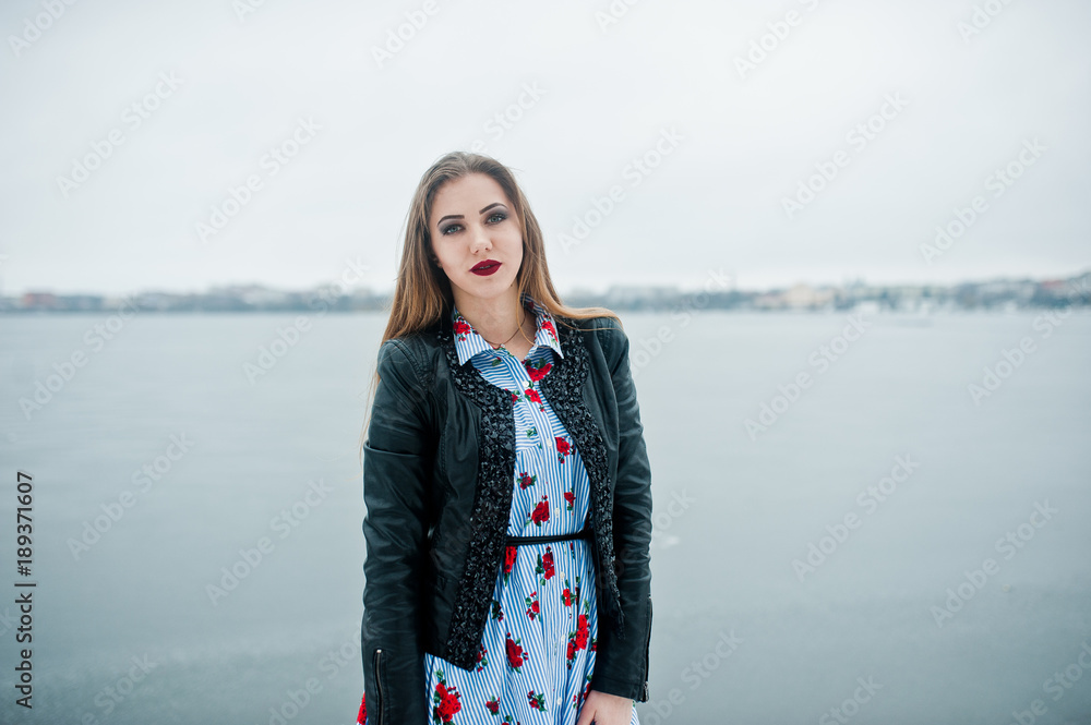 Stylish girl in leather jacket at winter day against frozen lake.