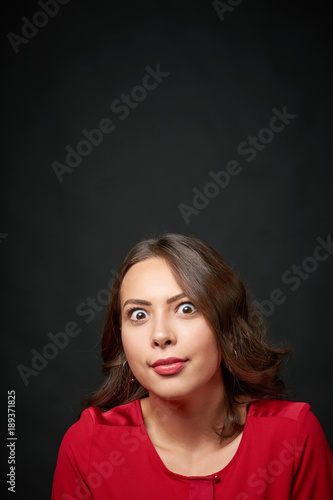 Surprised woman in red shirt and wavy hair looking up at blank copy space, over dark background