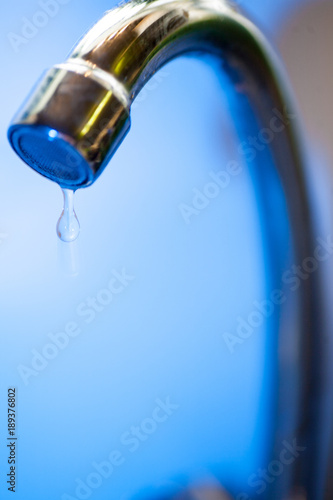 A stream of clean, transparent fresh water flows from the steel shiny tap into a stainless steel sink in blue tones. Water drains into the hole for the shell close-up macro