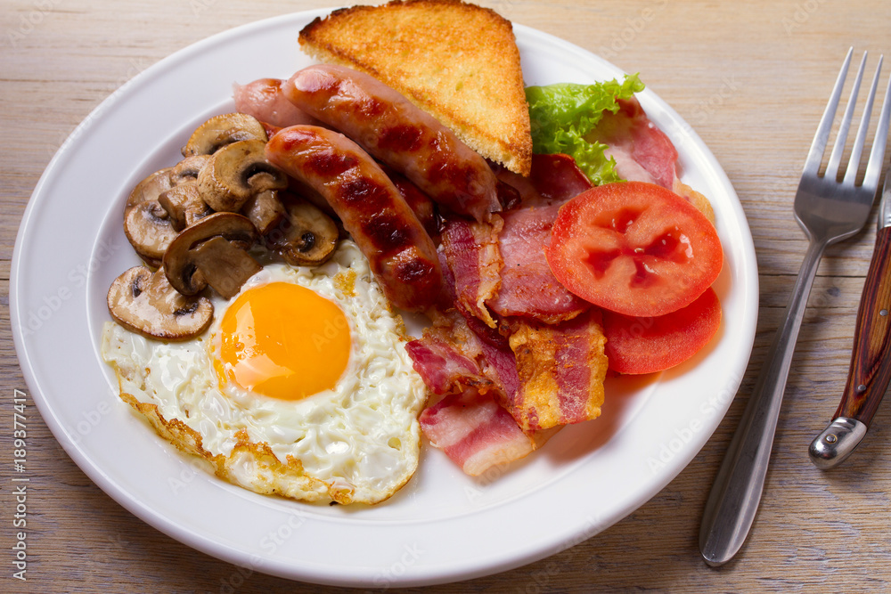 Traditional English or Irish breakfast: sausages, bacon, egg, mushrooms, tomatoes and toasts. Nutritious morning meal. horizontal Traditional English or Irish breakfast: sausages, bacon, egg, mushrooms, tomatoes and toasts. Nutritious morning meal. horizontal