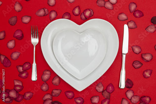 Heart shaped plate with knife and fork on a red background photo