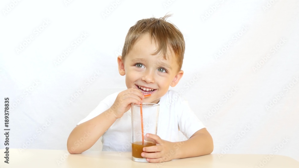 Happy child drinking juice through a straw for cocktails, sitting at a table and smiling on white background - 3 Happy child drinking juice through a straw for cocktails, sitting at a table and smiling on white background - 3