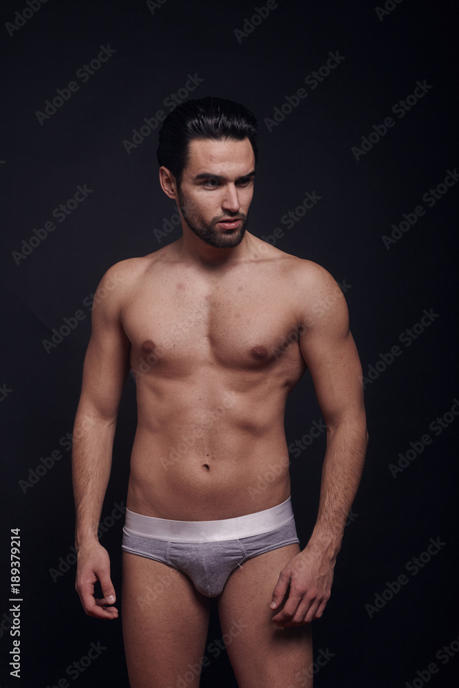 Fototapeta premium one young handsome man, looking away from camera, shirtless, fashion model, black background wearing briefs.