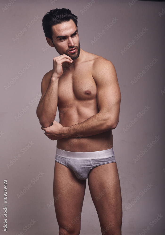 one young handsome man, looking away from camera, shirtless, fashion model, gray background wearing briefs.