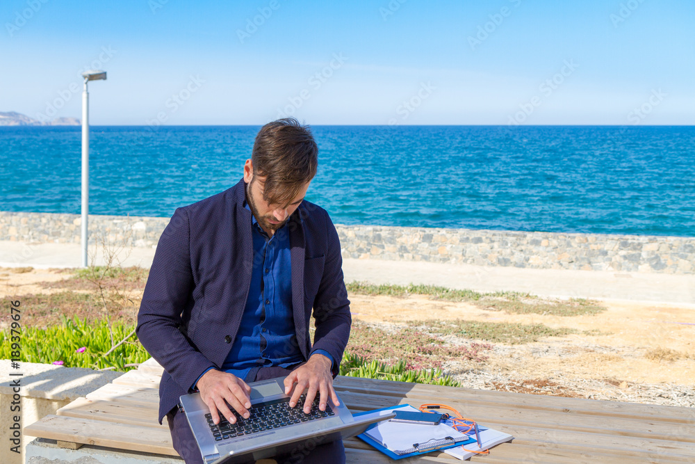 Young man using mobile devices phone and laptop by the ocean