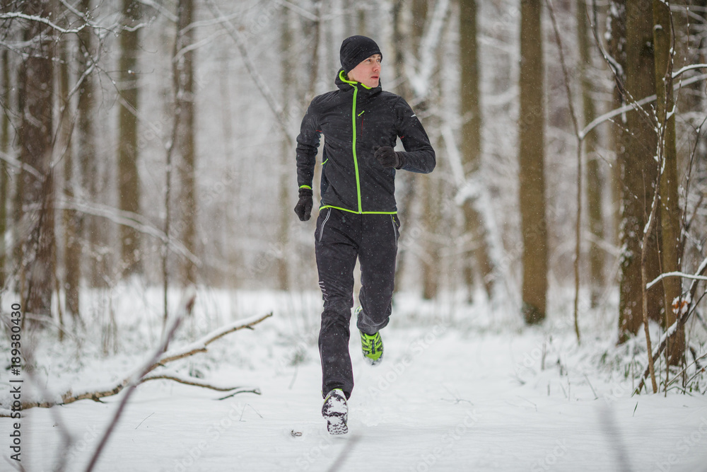 Photo of man in sportswear, black hat jogging in winter