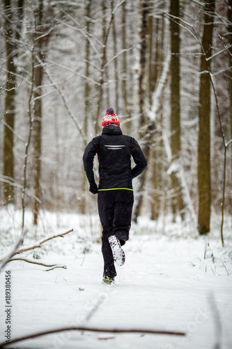 Photo from back of running athlete among trees in winter forest