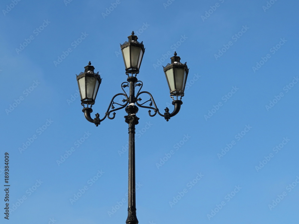 City street lantern on the background of blue sky. Vintage iron street lamp isolated