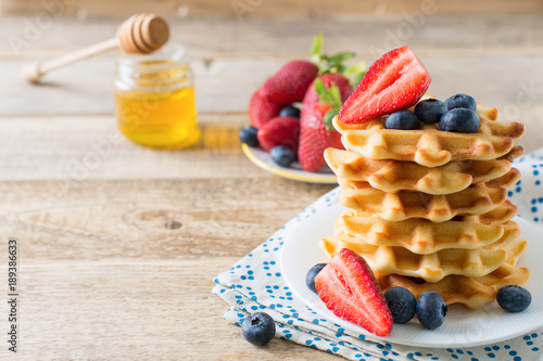 Stack of waffles with blueberries and strawberries on wooden background