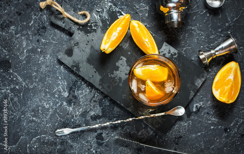 A glass of Negroni cocktail with orange and lemon. Alcoholic drink with rum and vermouth on dark stone table. photo