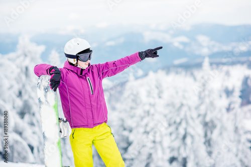 Portrait of a young woman snowboarder pointing with hand standing outdoors on the snowy mountains
