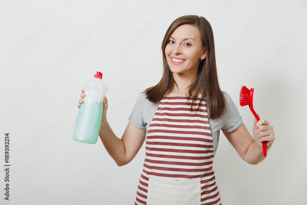 Young housewife in striped apron isolated on white background. Beautiful housekeeper woman holds bottle with cleaner liquid, pours on brush for washing dishes. Bottle with copy space for advertisement Young housewife in striped apron isolated on white background. Beautiful housekeeper woman holds bottle with cleaner liquid, pours on brush for washing dishes. Bottle with copy space for advertisement