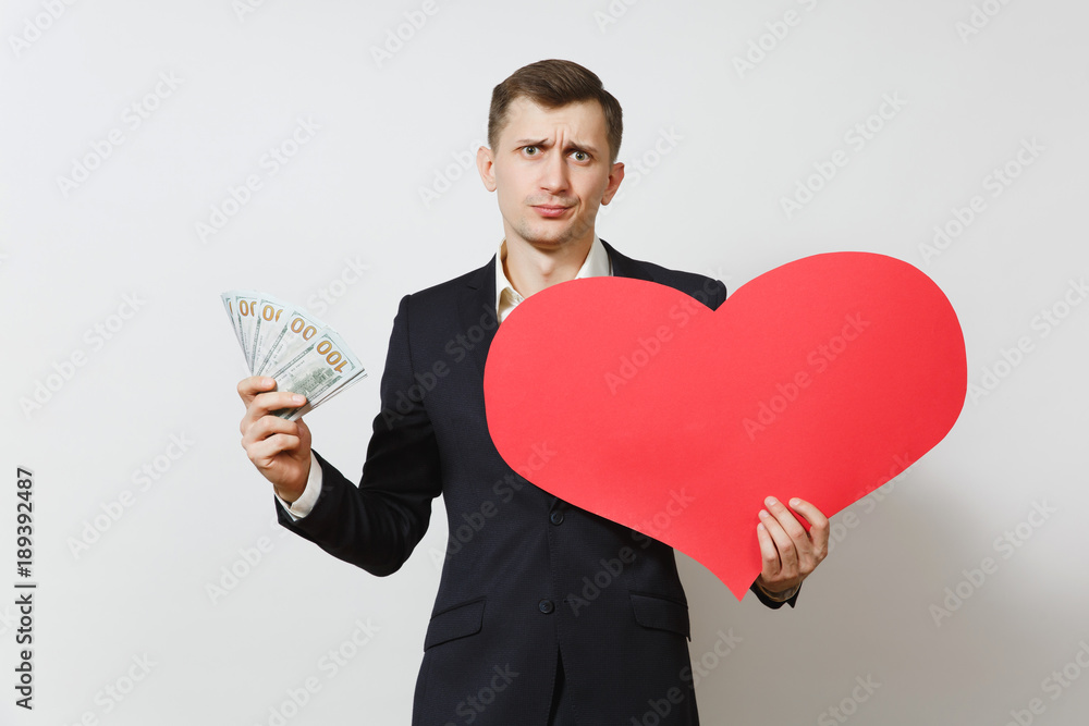 Dissatisfied man with big red heart, bundle of cash money dollars isolated on white background. Copy space for advertisement. St. Valentine's Day, International Women's Day, birthday holiday concept. Dissatisfied man with big red heart, bundle of cash money dollars isolated on white background. Copy space for advertisement. St. Valentine's Day, International Women's Day, birthday holiday concept.