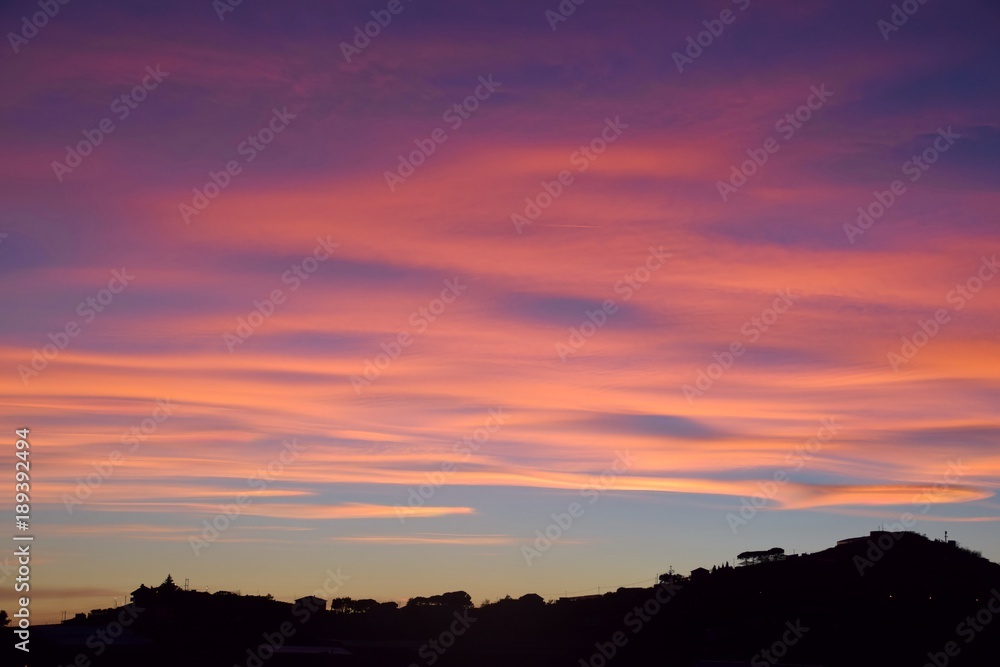 Tramonto con nuvole arancioni e rosa sulla collina