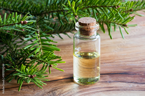 A bottle of fir essential oil with fir branches on a wooden table
