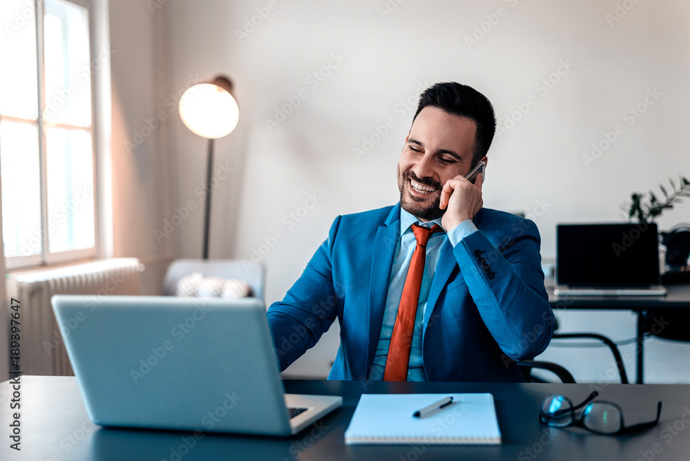 Young smiling businessmen working in his office and speaking on his mobile phone. Young smiling businessmen working in his office and speaking on his mobile phone.