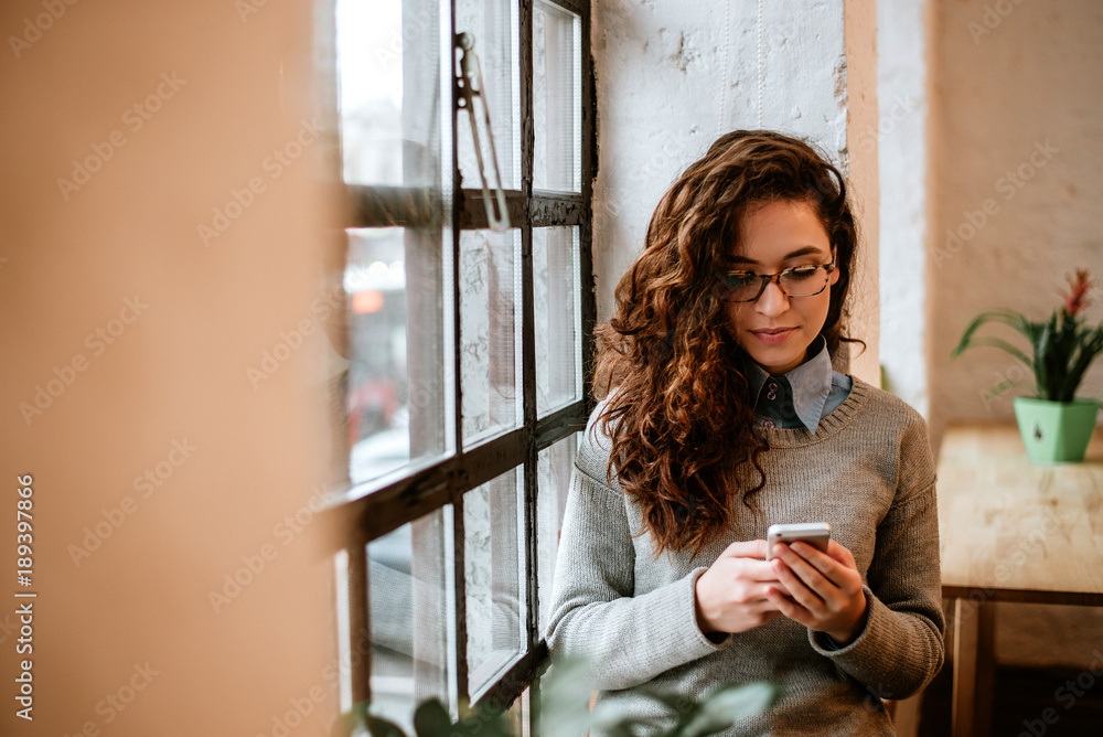 Portrait of a casual girl using a smart phone with a warm light near a window.