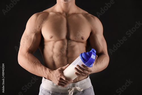 Handsome muscular young man with protein shake on black background