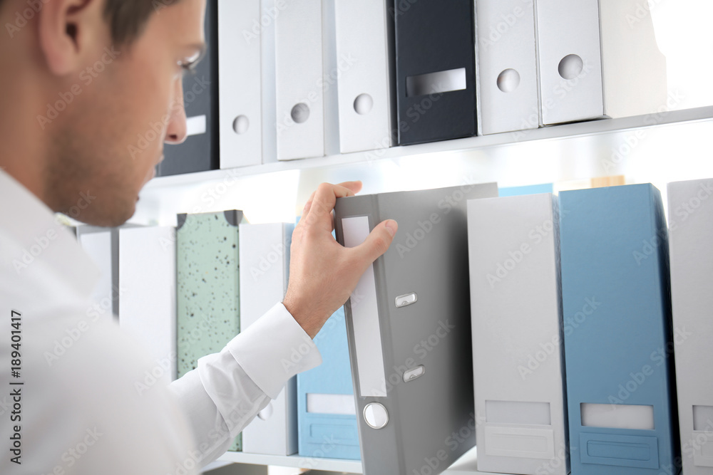Fototapeta premium Young man taking folder with documents from shelf in archive