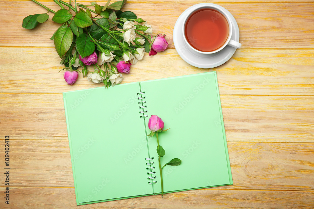 Roses, notebook and cup of tea on wooden background