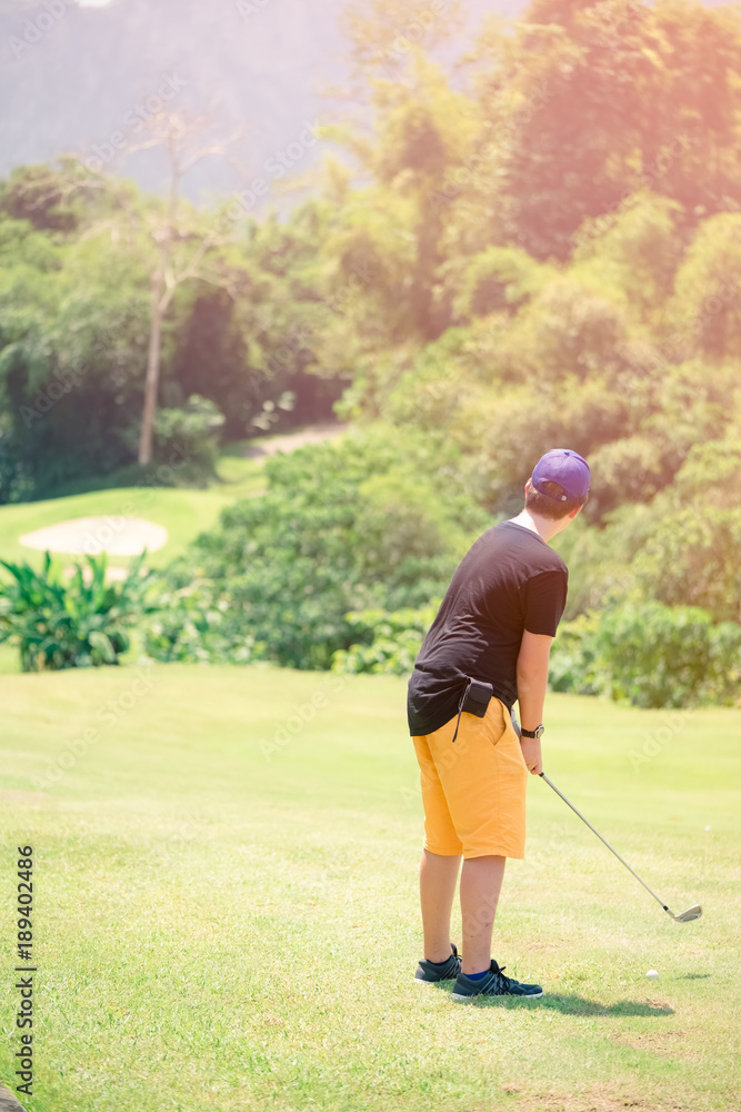 Golfer hitting golf shot with club on course while on summer vacation,boy playing golf on a golf course in the sun Golfer hitting golf shot with club on course while on summer vacation,boy playing golf on a golf course in the sun