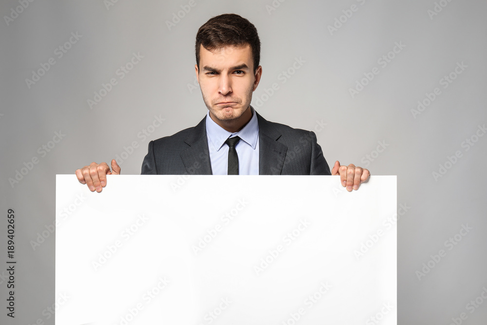 Emotional businessman with blank advertising board on grey background