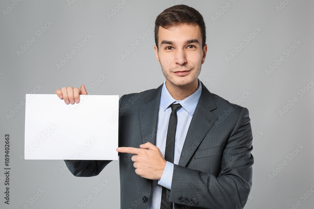 Handsome businessman with blank sheet of paper for advertising on grey background Handsome businessman with blank sheet of paper for advertising on grey background