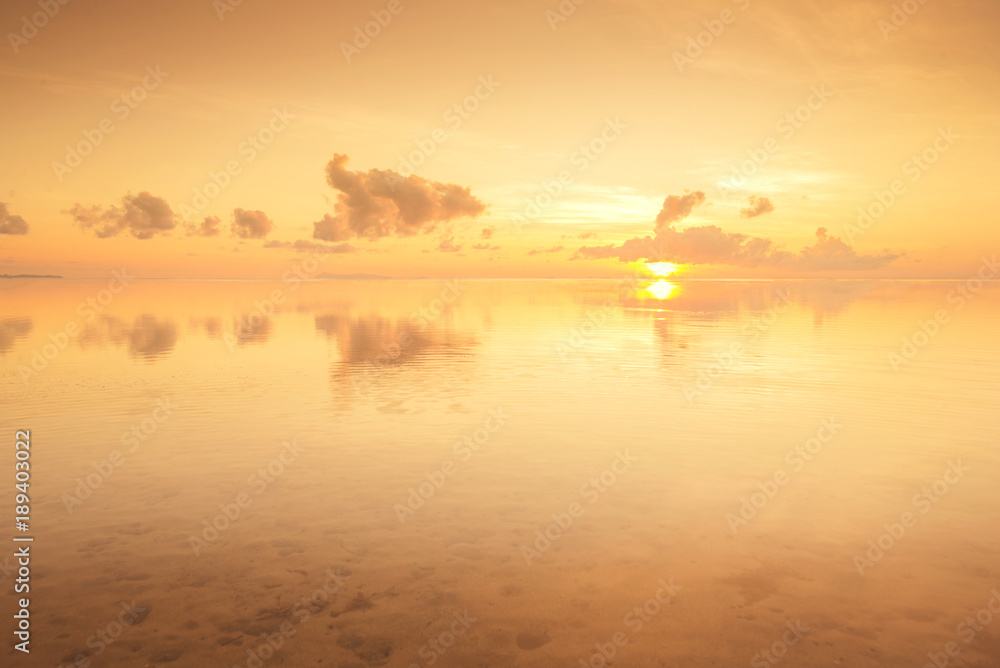 golden sunrise with reflection on a calm sea water.