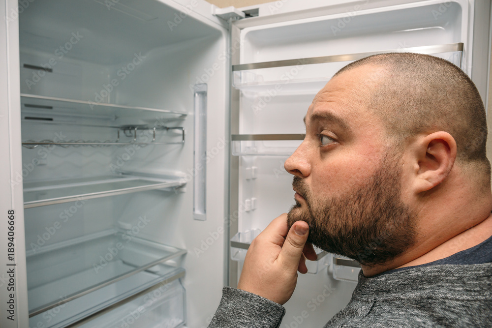 Funny fat man looking into empty fridge