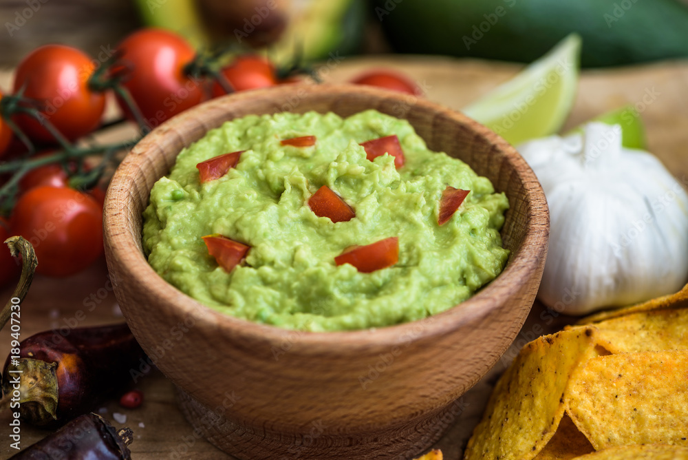 Guacamole in Wooden Bowl with Tortilla Chips and Ingredients Guacamole in Wooden Bowl with Tortilla Chips and Ingredients