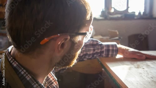 A stylish, young joiner sweeps the dust off the board and appreciates the quality of woodworking photo